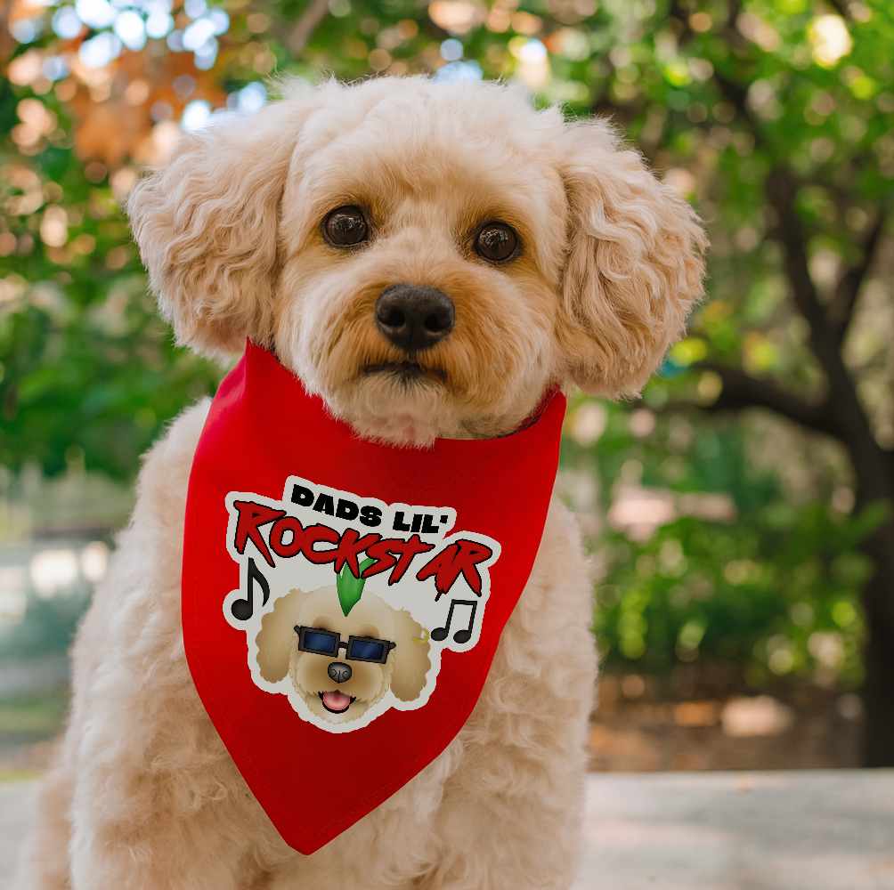 Dog wearing a red bandana with 'Dad's Lil' Rockstar' text and graphic, outdoors.